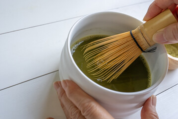 Woman Using Bamboo Whisk to Mix Matcha Green Tea Powder With Water