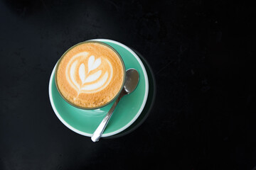 Hot Coffee Latte Top View There is a flower-shaped milk foam on a black table.