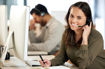 Take note of how expert customer care should be done. Portrait of a young businesswoman using a headset and writing in a notebook in a modern office.