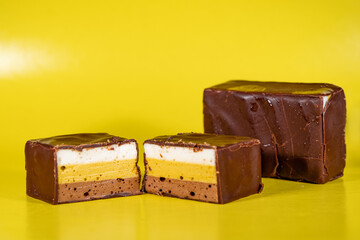 Sweets made of multi-colored souffle in white, yellow and brown, stacked in layers and covered with milk chocolate. Chocolate candies, stuffed with puff souffle.