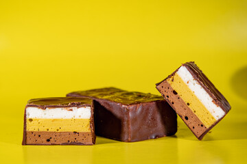 Sweets made of multi-colored souffle in white, yellow and brown, stacked in layers and covered with milk chocolate. Chocolate candies, stuffed with puff souffle.