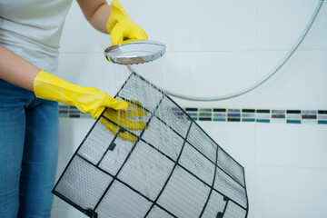 Asian woman cleaning a dirty and dusty air conditioning filter in her house. Housewife removing a...
