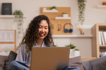 In the morning,Asian working woman relaxes on the sofa with her laptop, working from home.
