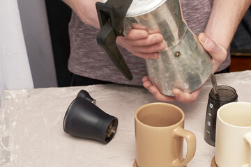 a man made coffee in a geyser next to mugs on the table