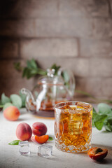 Glass of peach or apricot iced tea with fruit slices against white background