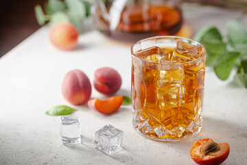 Glass of peach or apricot iced tea with fruit slices against white background