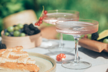 Outdoor summer lifestyle with a gourmet picnic laid out in a garden with berries, pie and pink drink in stylish glasses