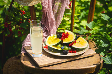 Outdoor summer lifestyle with a gourmet picnic laid out on a chair in a garden with berries, watermelon and yellow drink in stylish glasses