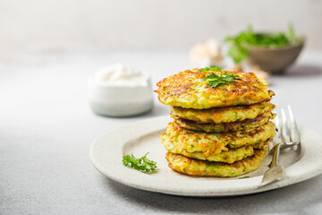 Fototapeta na wymiar Green zucchini fritters, vegetarian zucchini pancakes with fresh herbs and garlic, served with cream sauce on white background, selective focus