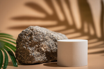 Creative concrete stone and round beige platform podium for cosmetics or products with shadowes of greens branches on beige background. Front view