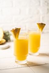 Pineapple cocktail or juice in two glasses with ice on white background with palm leaves