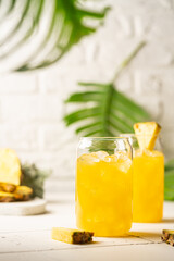 Pineapple cocktail or juice in two glasses with ice on white background with palm leaves