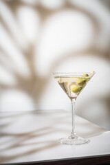 Cocktail vodka martini with green olives on light background with bright beautiful shadows