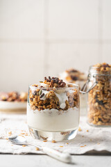 Crunchy granola with yogurt, banana, nuts, chocolate and honey in a glass on white background. Healthy breakfast concept.