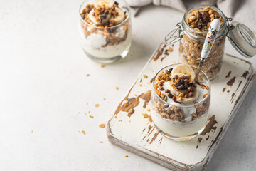 Crunchy granola with yogurt, banana, nuts, chocolate and honey in a glass on white background. Healthy breakfast concept.