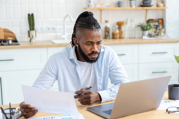 Portrait of focused African American businessman freelancer analyzing annual sales chart working remotely from home