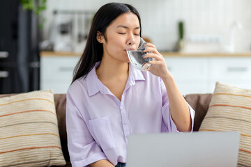 Portrait of young female freelancer drinking clean water sitting at workplace at home on the couch
