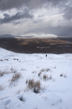 Epic Winter landscape image from mountain top in Scottish Highlands down towards Rannoch Moor during snow storm and spindrift off mountain top in high winds