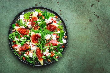 Delicious summer salad with figs, feta cheese, walnuts, arugula and sweet  jam dressing on rusty green table background, top view, negative space