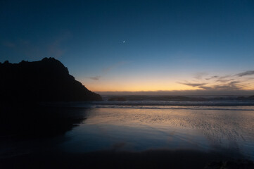 Rocks in the surf of Pfeiffer beach, around sunset. Deep yellow orange clouds color the sky.