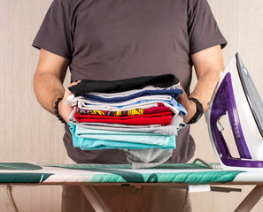 a man holds a stack of ironed laundry against the background of an ironing board and an iron