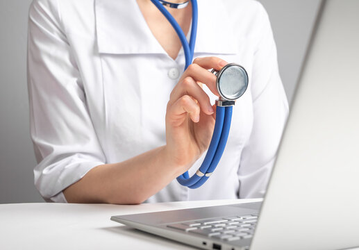Doctor with stethoscope speaking to patient through video chat. Woman in lab coat advising client with illness, injury, using laptop. Online medicine consultation and diagnostics concept. photo