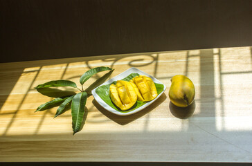 Ripe mangoes are placed on a plate on the table with a bouquet of leaves.
