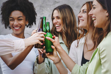 Four young multiethnic girlfriends making a toast with beer bottles while having fun standing...