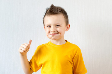 a boy in a yellow T-shirt got chocolate stained after eating a donut. Cute happy boy smeared with chocolate around his mouth.