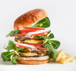 Big burger with beef patty, lettuce, tomato, cheese, sauce and fries at white background. American fast food with cheeseburger. To go food for lunch. Front view
