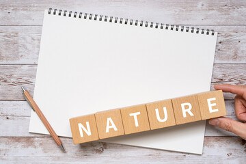 「NATURE」と書かれた積み木、ノート、ペン、手