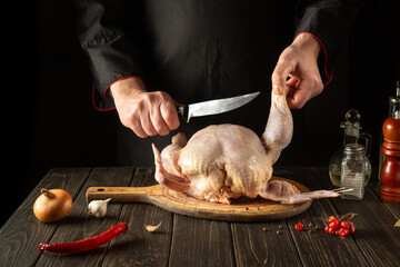 A professional chef cuts raw chicken with a knife in the kitchen. Cooking chicken for lunch. European cuisine