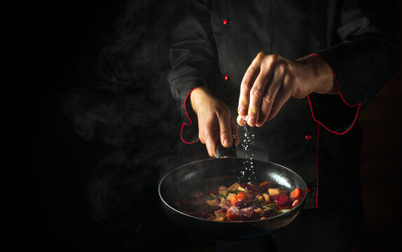Cooking fresh vegetables. The chef adds salt to a steaming hot pan. The idea of European cuisine for a hotel with advertising space.