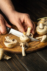 Slicing Agaricus mushrooms on a cutting board by the hands of a chef using a knife to prepare a delicious national dish