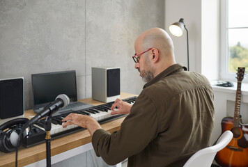 Back view of middle-aged male musician play electronic keyboard sing in microphone record music....