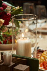 a large white candle burns in a transparent candlestick on a festive table decorated with floral decor