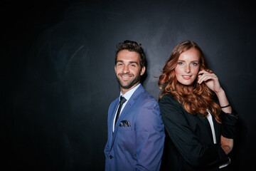 Business is what we do. Studio portrait of a young couple standing against a dark background.