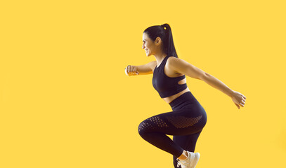 Fototapeta na wymiar Beautiful smiling female athlete running and jumping isolated on vivid yellow background. Side view of young sportswoman in stylish black sports uniform running looking at copy space. Banner.