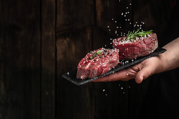 Chef salts steak in a freeze motion with rosemary and spices. Preparing fresh beef or pork on a dark background. Long banner format