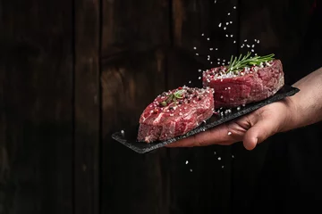 Fotobehang Chef salts steak in a freeze motion with rosemary and spices. Preparing fresh beef or pork on a dark background. Long banner format © Надія Коваль