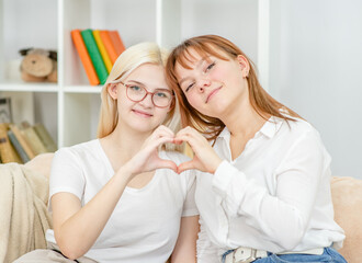Two smiling young girls show heart sign. LGBT concept