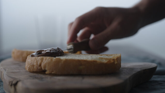 man spreading chocolate hazelnut spread on ciabatta slice on olive wood board