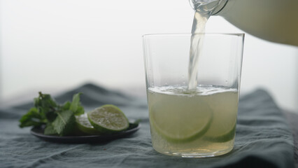 Man pour lemonade in tumbler glass with lime slices on wood table
