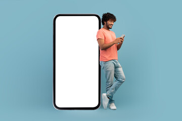 Cool indian guy leaning on huge smartphone, using cell phone