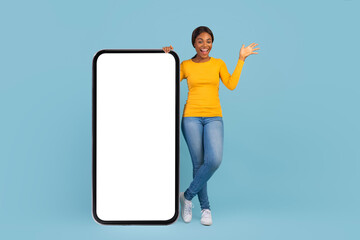Smiling emotional pretty millennial african american woman in casual stand with big smartphone with blank screen