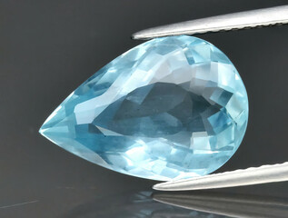 Natural gemstone blue aquamarine in tongs on a gray background