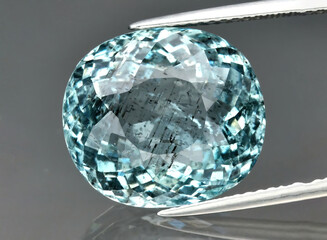 Natural gemstone blue aquamarine in tongs on a gray background