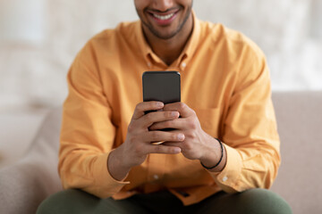 Obraz na płótnie Canvas Smiling young man using smartphone at home, close up