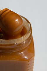 brown honey with a wooden spoon in a transparent glass jar on a white background close up.buckwheat honey