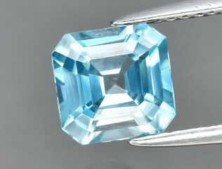 Natural gemstone blue zircon in tongs on a gray background